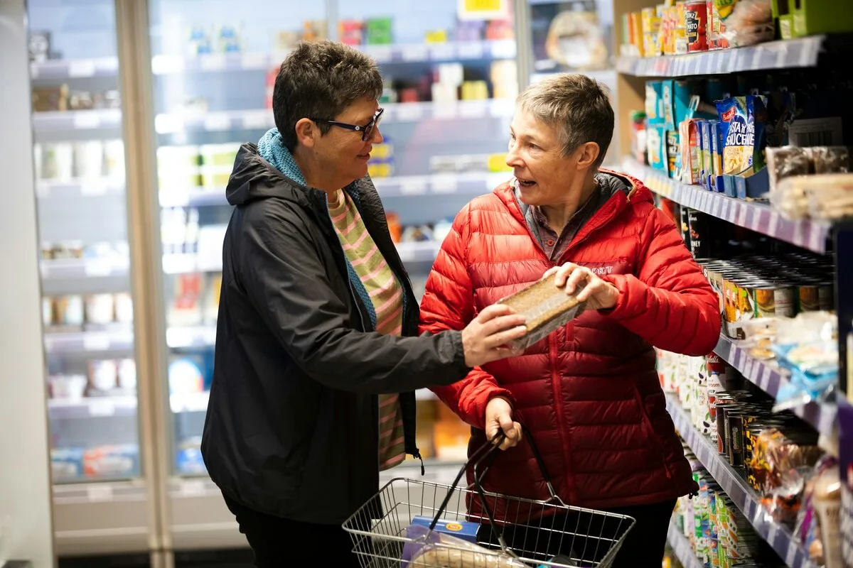 Zwei Frauen stehen im Supermarkt und sehen sich gemeinsam eine Packung an